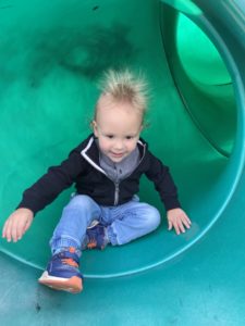 A toddler at the bottom a green slide enjoying fall activities in OKC