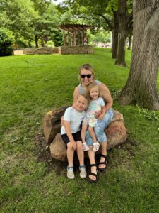A mom with her preschool-aged son and toddler daughter sitting outside under a tree.
