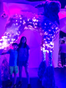 Two kids standing under a giant long-legged bunny statue at Factory Obscura.