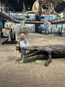 A young girl posing with a crocodile at SKELETONS: Museum of Osteology.